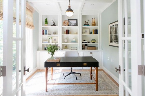 Chic-home-office-features-a-black-bamboo-desk-and-swivel-chair-placed-in-front-of-a-wall-of-floor-to-ceiling-built-in-shelves-and-cabinets