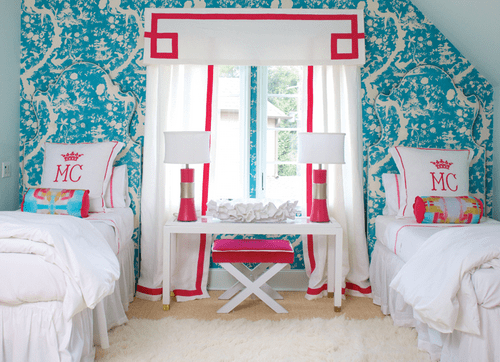 Pink-and-turquoise-blue-girls-bedroom-features-an-accent-wall-clad-in-turquoise-toile-wallpaper-lined-with-twin-beds-without-headboards-dressed-in-white