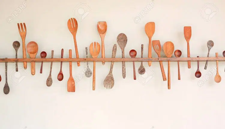Decorative set of wooden kitchen utensils hanging on white wall background.